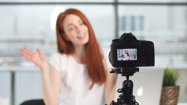 Young beautiful blogger girl working in office while shooting on camera