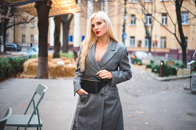 Young beautiful blond woman in an autumn coat stands on a city street. Soft focus. Fashionable concept. Gray background