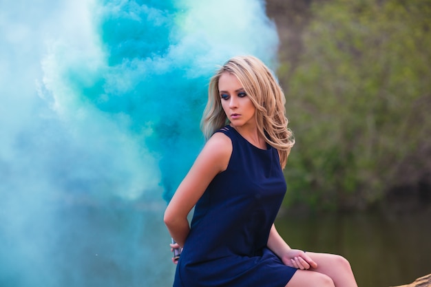 Young beautiful blond woman in blue mini dress and floral wreath standing. Smoke background.