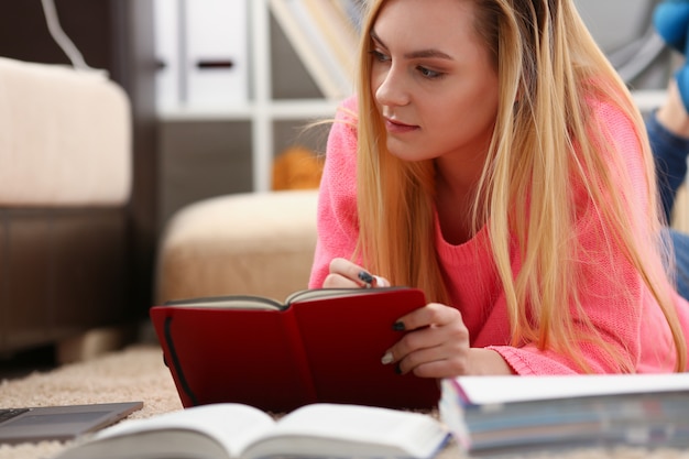 本を読んで床に横になっている若い美しいブロンドの女性