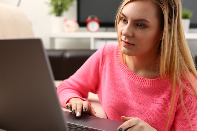 La giovane bella donna bionda si siede nel lavoro del soggiorno sul laptop