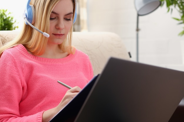 Foto la giovane bella donna bionda si siede sul sofà nel raccoglitore della tenuta del salone nel lavoro di armi con il computer portatile ascolta musica