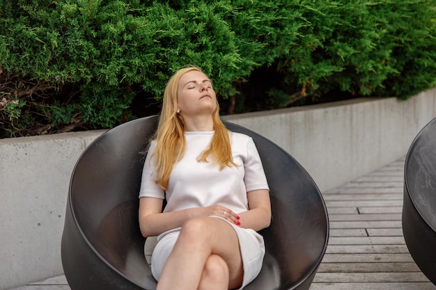 Young beautiful blond woman sitting outdoors on the wooden terrace in the city and resting Girl has break spending time outside and relaxing Time with yourself dreaming relaxation mental health