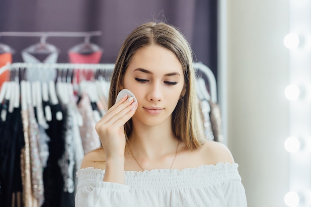 A young beautiful blonde girl makes her own make-up in front of the mirror