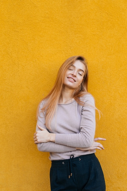 Young beautiful blonde girl posing on yellow wall background, smiling, street style