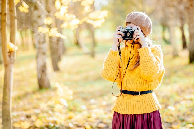 Young beautiful blonde girl with vintage camera have rest in the park in autumn season time.