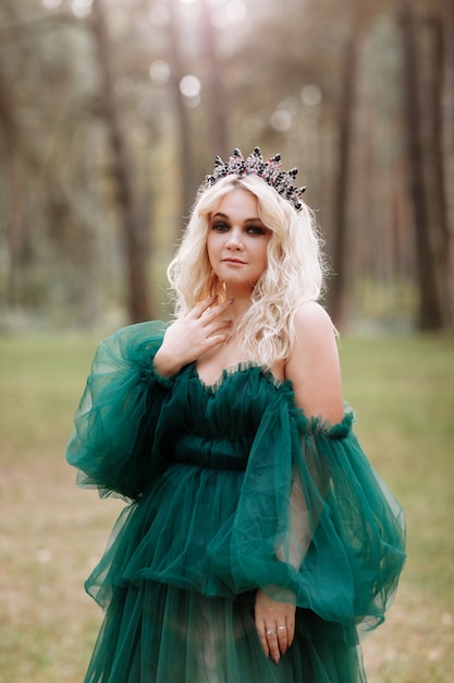 Young beautiful blonde hair woman queen. Princess walks. autumn green forest mystic. Vintage medieval shiny crown.