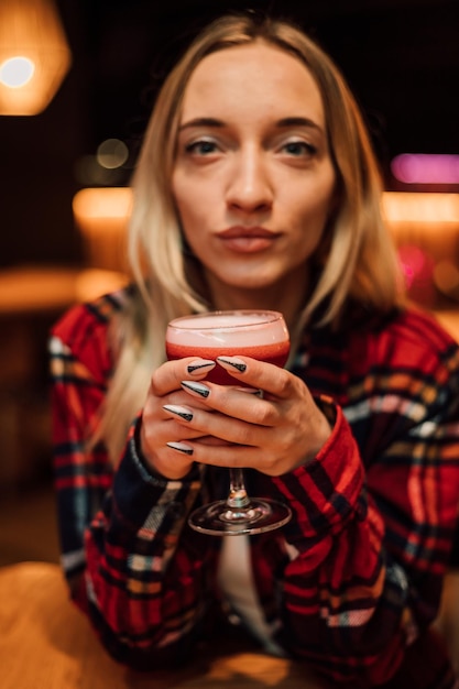 A young beautiful blonde holds a glass with a cocktail in a restaurant