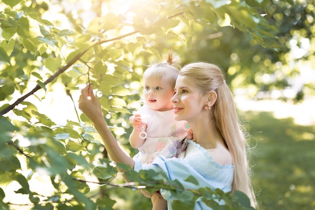 Молодая красивая блондинка мать с ее девочкой смеются вместе и играют в зеленом парке