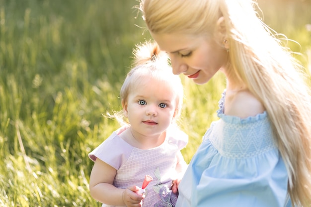 Young beautiful blonde mother with her baby girl laughing together and playing in green park