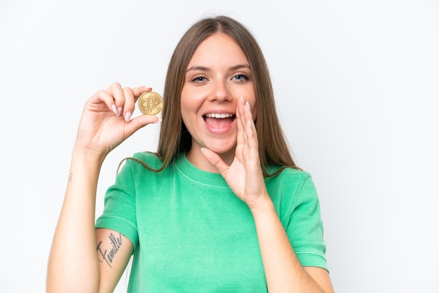 Young beautiful blonde woman holding a Bitcoin isolated on white background shouting with mouth wide open