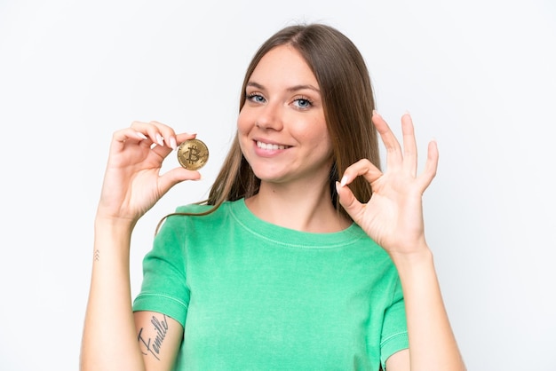 Young beautiful blonde woman holding a Bitcoin isolated on white background showing ok sign with fingers