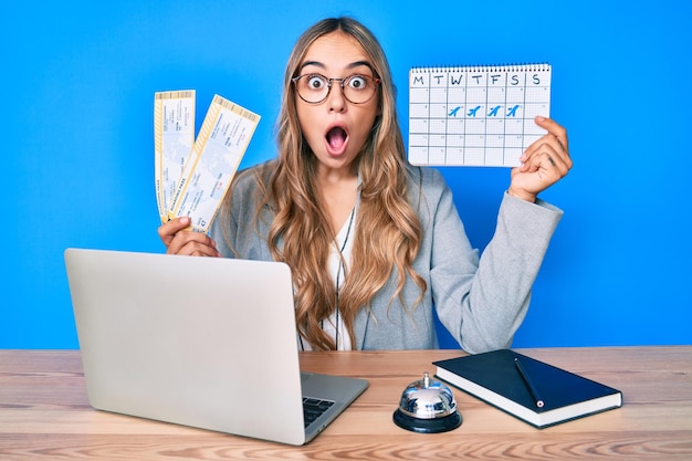 Young beautiful blonde woman holding boarding pass and travel calendar afraid and shocked with surprise and amazed expression fear and excited face