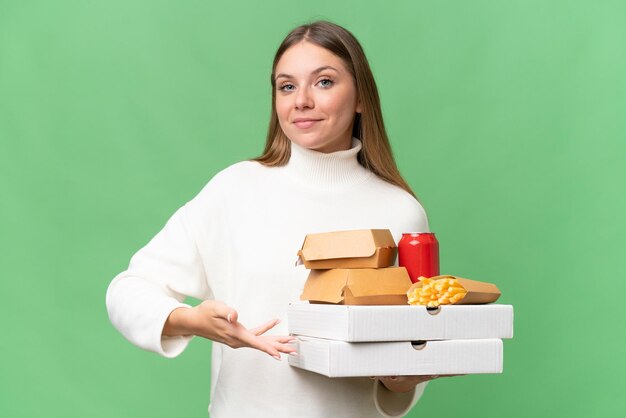 Young beautiful blonde woman holding takeaway food over isolated background extending hands to the side for inviting to come