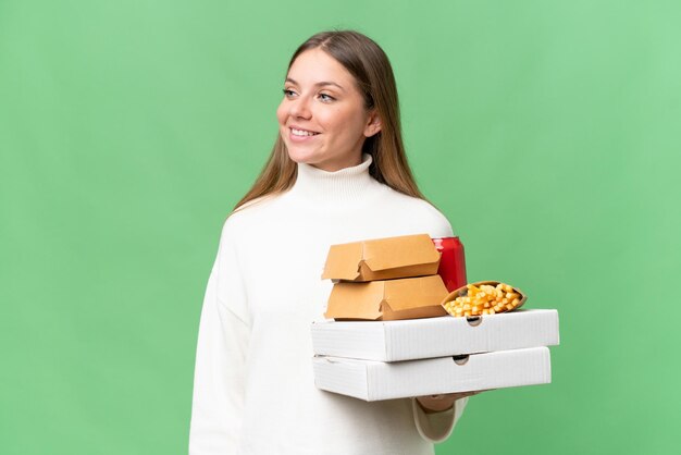 側を見ている孤立した背景の上にテイクアウトの食べ物を保持している若い美しいブロンドの女性