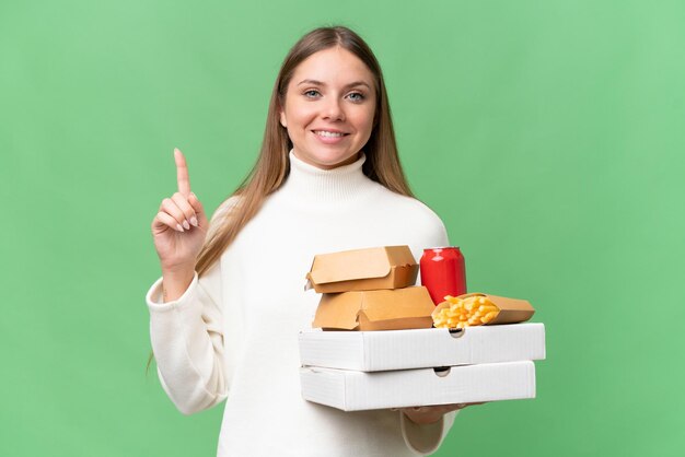 素晴らしいアイデアを指している孤立した背景の上に持ち帰り用の食べ物を保持している若い美しいブロンドの女性