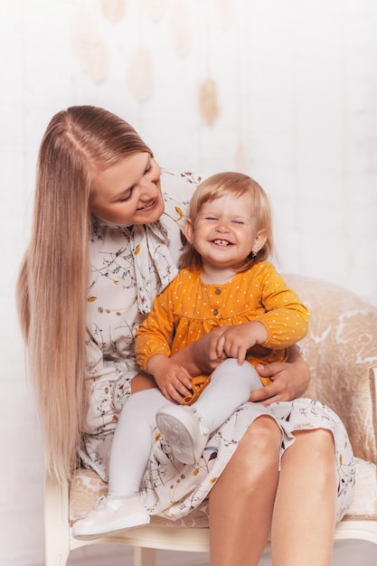 Young beautiful blonde woman is holding a little daughter on her lap. Vertical