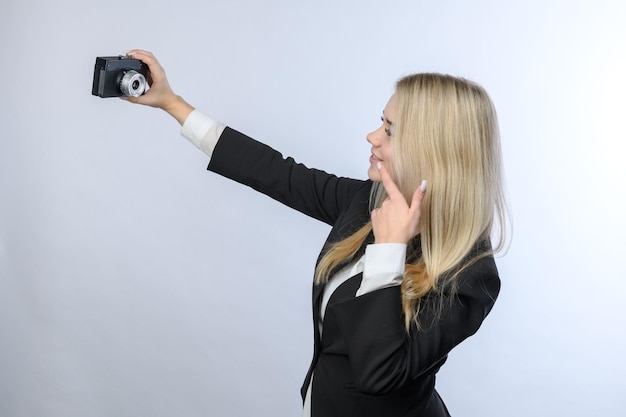 Young beautiful blonde woman making selfie by retro camera on white background