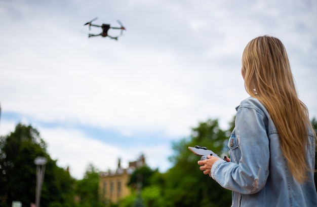 Giovane bella donna bionda che pilota un drone con un telecomando in mano