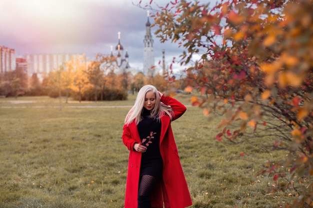 Foto giovane bella donna bionda in cappotto rosso nel parco d'autunno