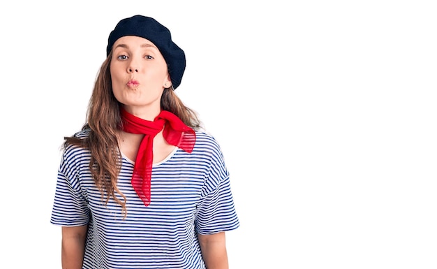 Photo young beautiful blonde woman wearing french beret and striped tshirt looking at the camera blowing a kiss on air being lovely and sexy love expression