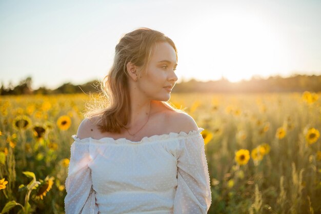 Молодая красивая блондинка в белом платье в поле подсолнухов на закате Вечерние солнечные лучи Лето