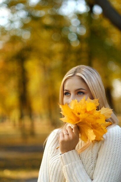 Young beautiful blonde woman in a white sweater walks in the autumn park