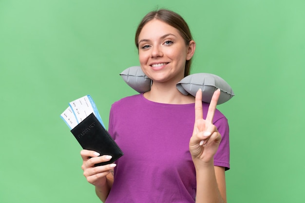 Young beautiful blonde woman with Inflatable travel Pillow over isolated background smiling and showing victory sign