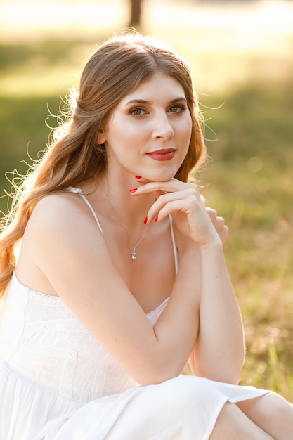 Giovane bella donna bionda con capelli lunghi in abito bianco in natura