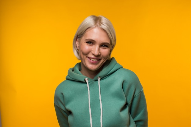 Young beautiful blonde woman with a short haircut in green hoodie looks happy