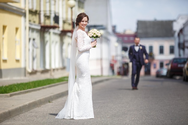 Young beautiful bride girl with wedding bouquet of roses stands on the street the wind blows the veil