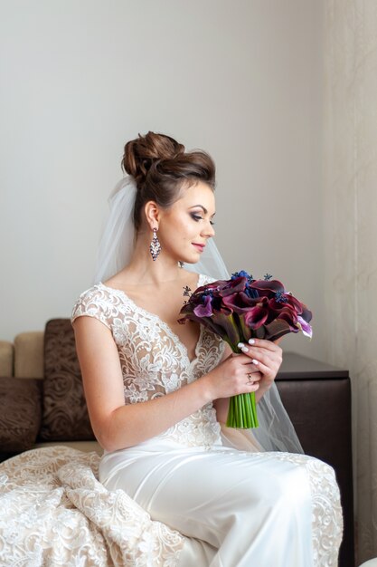 Young beautiful bride holds a bouquet of dark purple callas.