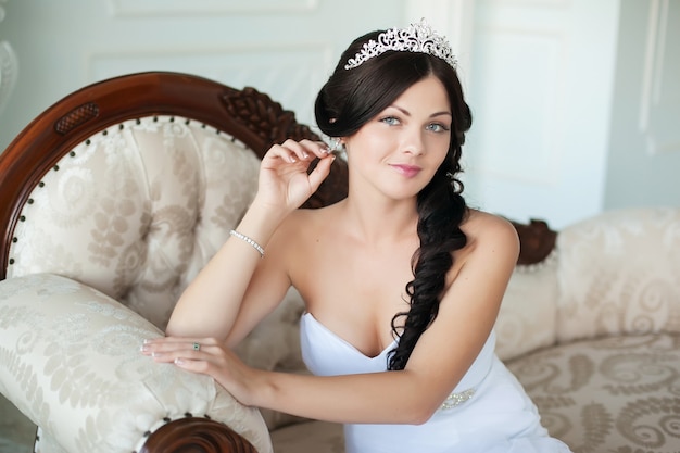 Young beautiful bride sits on an elegant sofa and looking at the camera