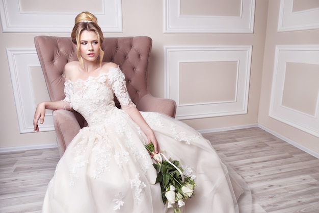 Giovane bella sposa. acconciatura da sposa, capelli biondi, abito da sposa, trucco e bouquet della sposa. tiro al coperto