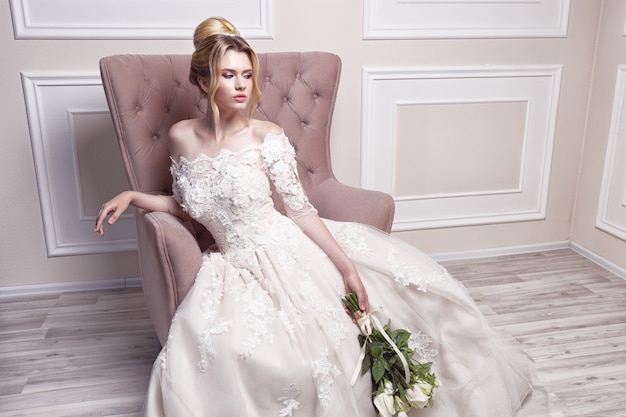 Young beautiful bride. Wedding hairstyle, blond hair, wedding dress, makeup and bride's bouquet. Indoor shot