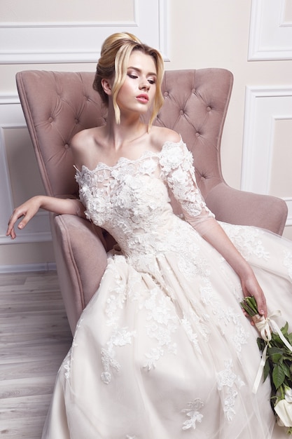 Giovane bella sposa. acconciatura da sposa, capelli biondi, abito da sposa, trucco e bouquet della sposa. tiro al coperto