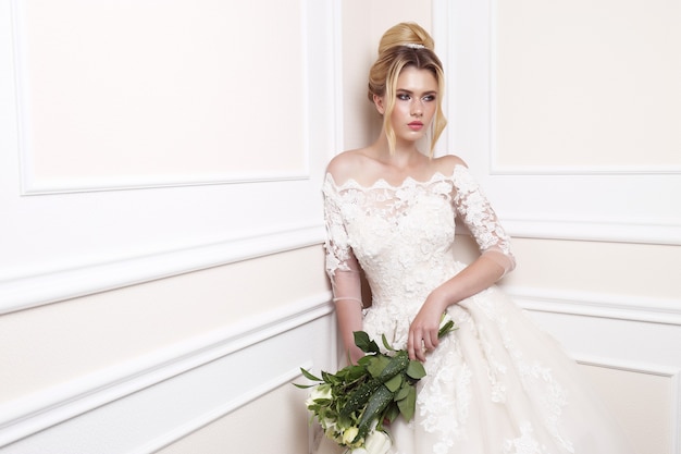 Young beautiful bride. Wedding hairstyle, blond hair, wedding dress, makeup and bride's bouquet.