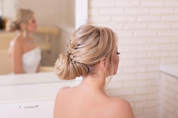 Young beautiful bride with blonde wedding hairstyle and makeup in hairdressing salon