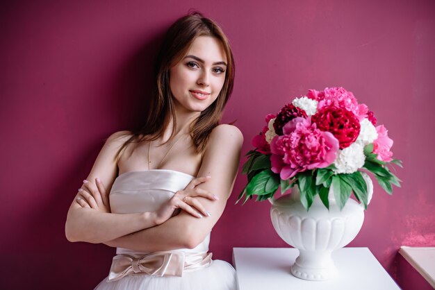 Young beautiful bride with a bouquet of pink peony near the wall