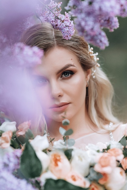 Young beautiful bride with a wedding bouquet near lilac bushes