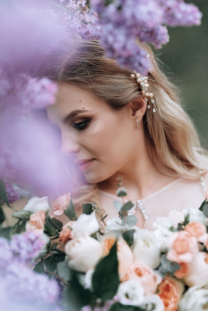 Young beautiful bride with a wedding bouquet near lilac bushes