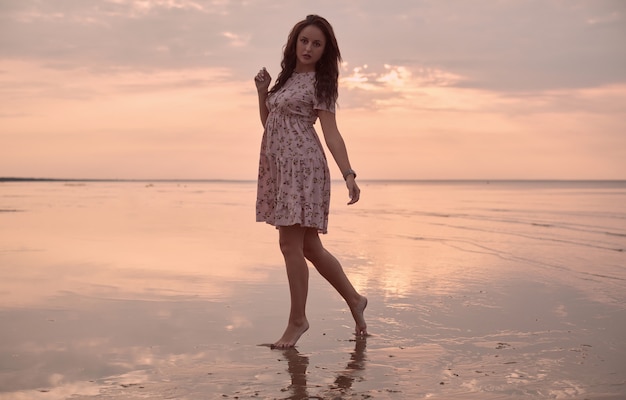 Young beautiful bright girl in a summer dress walking in the sunset