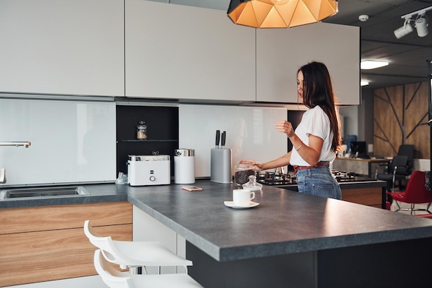 Young beautiful brunette in casual clothes preparing coffee in kitchen at daytime