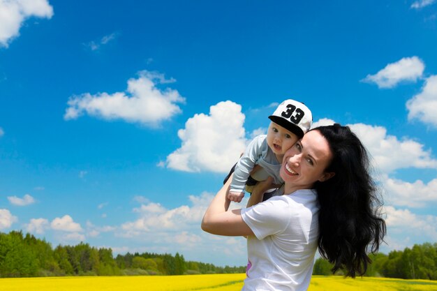 黄色い菜の花畑で幼い息子を抱きかかえた、若くて美しいブルネットの母親。