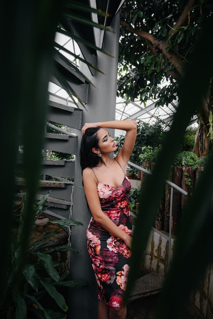 Photo a young beautiful brunette poses near a spiral staircase in the botanical garden among the dense thickets of the tropic forest. spa