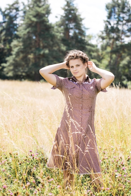 Young beautiful brunette with braid on her head in a country style dress on the field