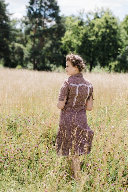 Young beautiful brunette with braid on her head in a country style dress on the field