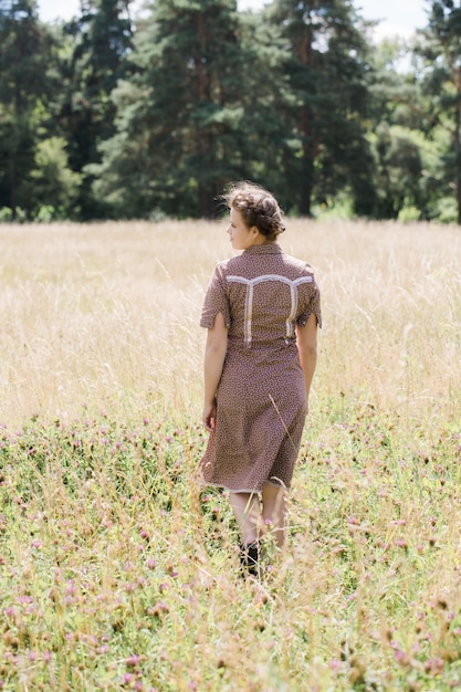 Young beautiful brunette with braid on her head in a country style dress on the field