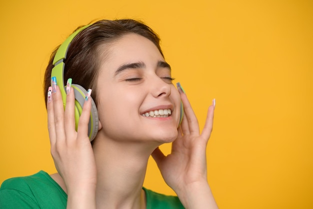 Young beautiful brunette with a short haircut enjoys listening to music on wireless headphones