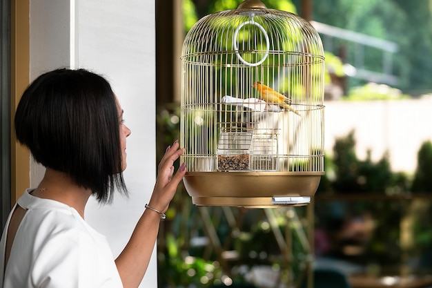 young beautiful brunette woman in a bar admiring a canary bird in a golden cage